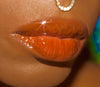 Close-up of a person's lips with glossy chocolate brown lipgloss, blurred background