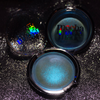 Three round makeup compacts on a sparkly black background. One compact is open, showing a shimmering light blue pressed powder.