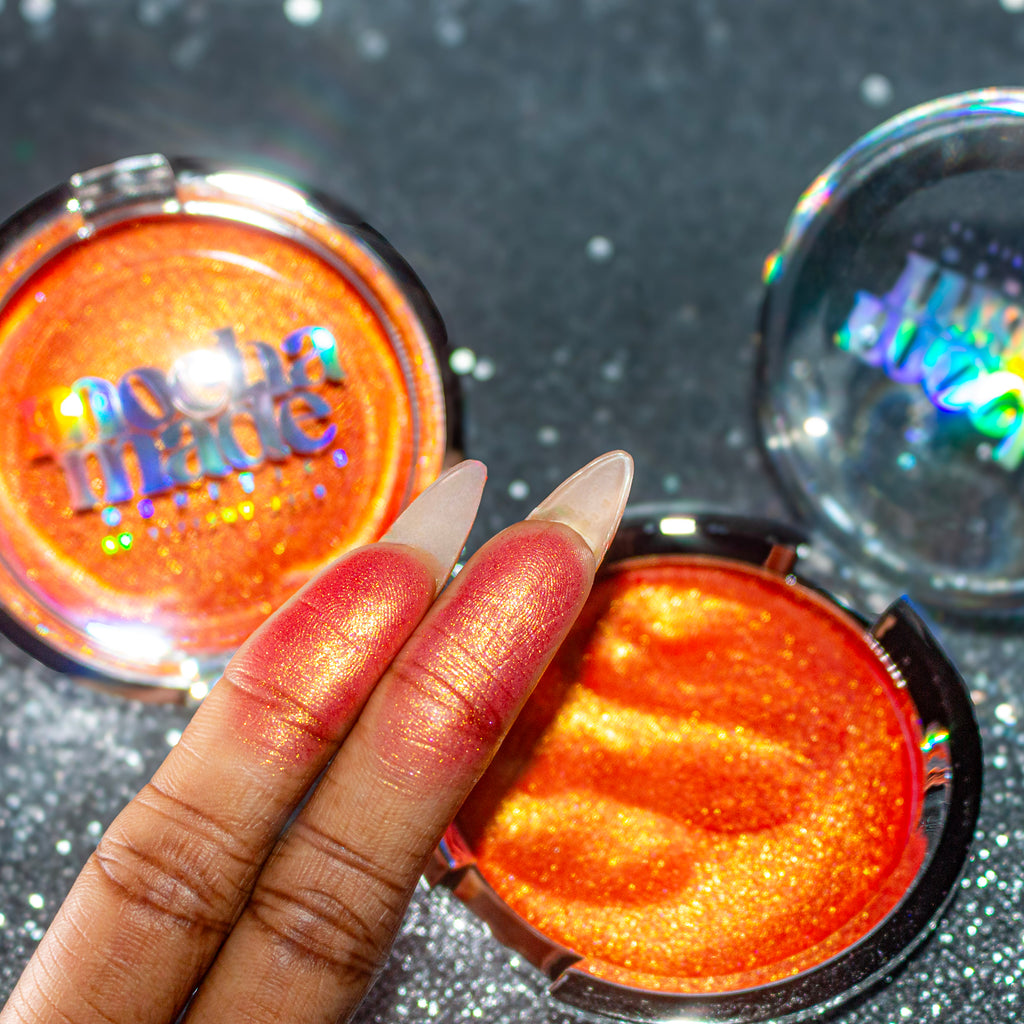 Shimmering molten tangerine golden chrome highlighter makeup compact with 'mocha made cosmetics' branding on a glittery background