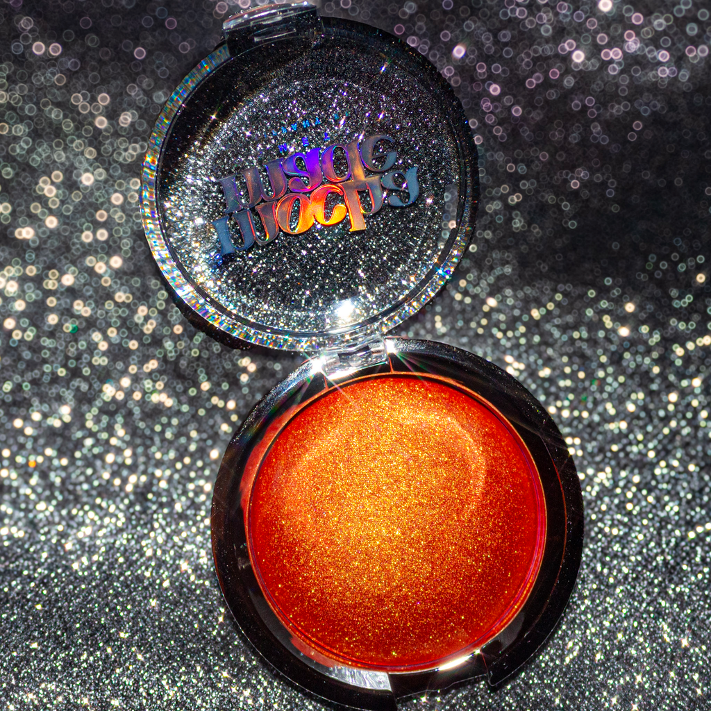 Shimmering molten tangerine golden chrome highlighter makeup compact with 'mocha made cosmetics' branding on a glittery background