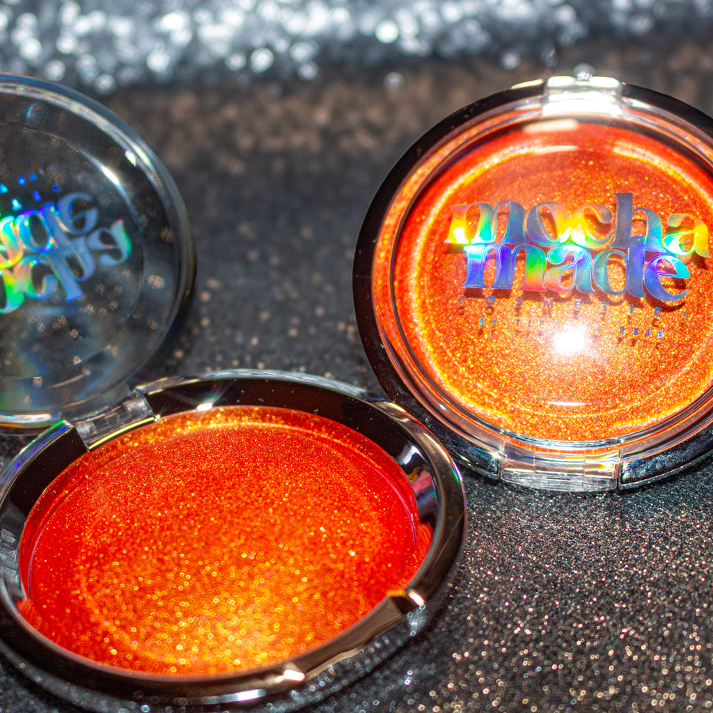 Shimmering molten tangerine golden chrome highlighter makeup compact with 'mocha made cosmetics' branding on a glittery background