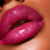Extreme close-up of a person's lips wearing a highly glossy, sparkly magenta-pink lip gloss with fine glitter.