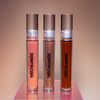 Three lip gloss tubes from Mocha Made Cosmetics on a reflective surface with a gradient background.