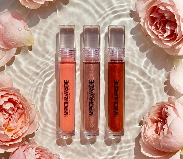 Three lip gloss tubes from Mocha Made Cosmetics on a reflective surface with a gradient background.
