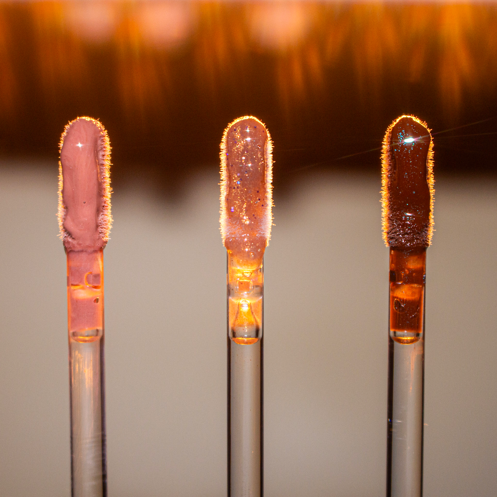 Three lip gloss tubes from Mocha Made Cosmetics on a reflective surface with a gradient background.